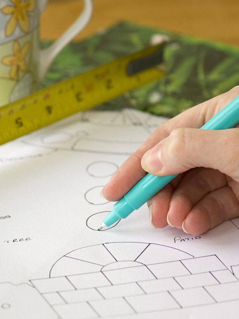 A gardener draws a garden plan using a pen and a ruler.