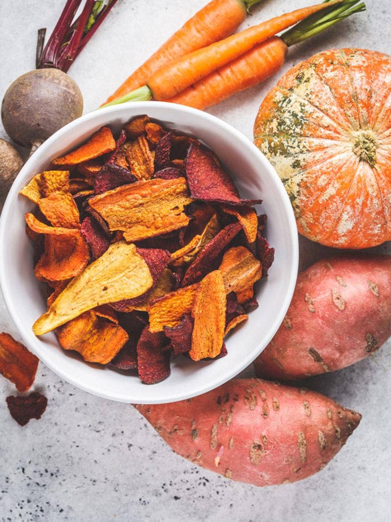 A bowl of dehydrated vegetables surrounded by fresh vegetables