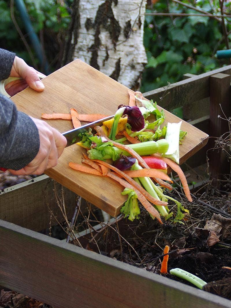 A person adding vegetable scraps to a compost bin.