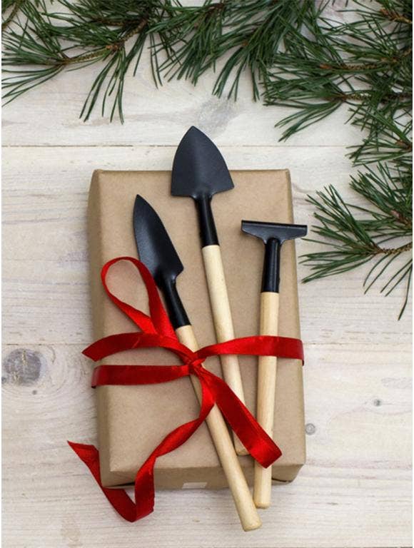 A wrapped present with gardening tools on top tied with a red ribbon.